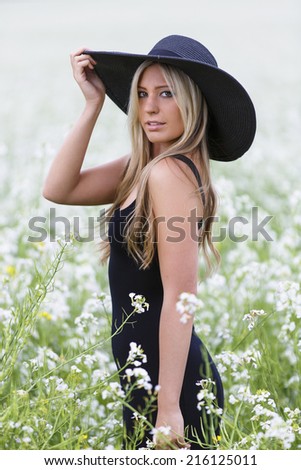 Gorgeous and young looking model posing with one arm up on her black hat