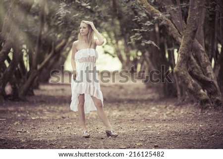 Beautiful model posing in the forest wearing a white dress and looking at the beam of light