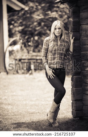 Old fashion portrait of a young lady posing next to an old timber cabin and barn area