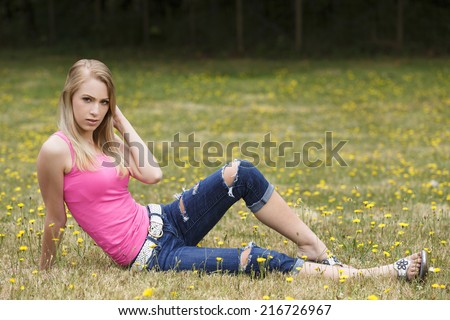 Young girl laying on the lawn and posing in pink tank top and wearing white belt and ripped denim jeans pants