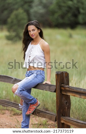 Young slim brunette model smiling and sitting on a fence