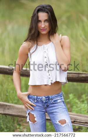 Fit brunette model in ripped jeans and white loose top posing with a sassy smile