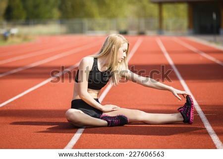 Determine young blond athlete warming up and stretching her legs