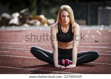 Beautiful blond girl streching her legs on the running track