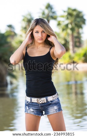 Sassy and young blond girl in black tank top and short denim shorts with white belt