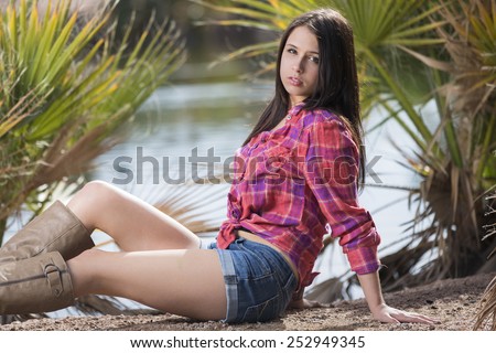 Young teen brunette laying down outdoors in red tied up flannel shirt