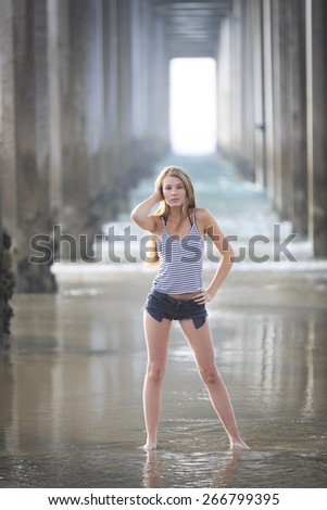 Young woman posing with long legs under a bridge and in shadow water