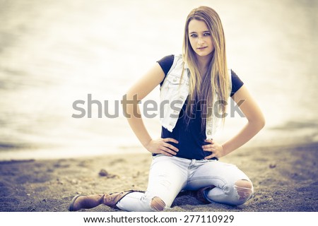 Young blond girl sitting on the beach with ripped jeans and black shirt