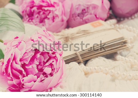 fresh pink  peonies with pile of old mail on white lace background, retro toned