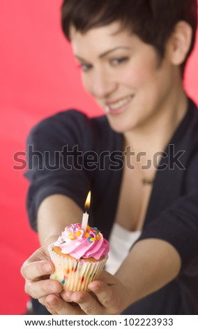 A pretty brunette woman holds her birthday cupcake one burning candle vertical