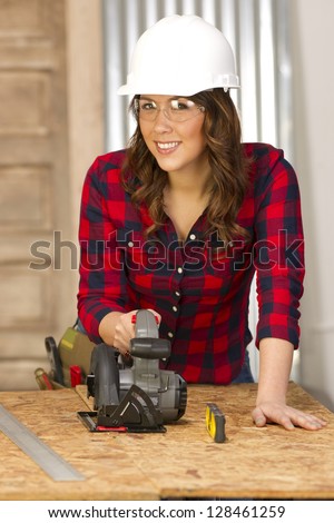 A female handy woman works on a building project in the shop sawing cutting boards