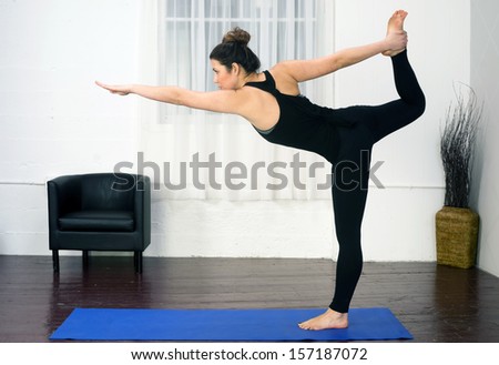 Woman practices Yoga in Studio on Blue Mat utilizing standing pose