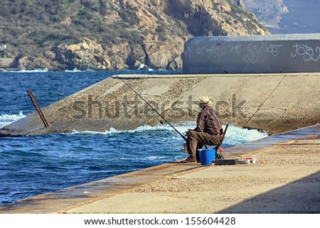 older man fishing on the shores of the sea with a cane