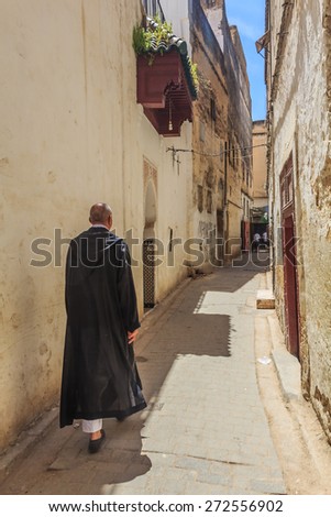 Fes, Morocco - May 11, 2013: Man in djellaba, berber clothing walking down a street in Fes Medina in Morocco3: Man in djellaba, berber clothing walking down a narrow street in Fes Medina in Morocco