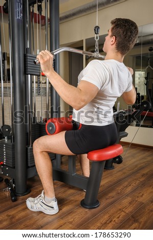 Handsome young man doing B lats pull-down workout in gym