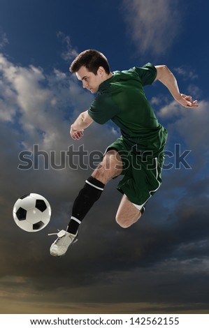 Soccer player kicking the ball with clouds on a the background