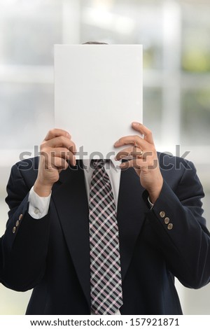 Businessman holding a blank paper and covering his face