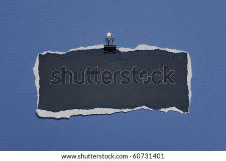 Piece of Rip Paper with white edges on a clip against a blue background