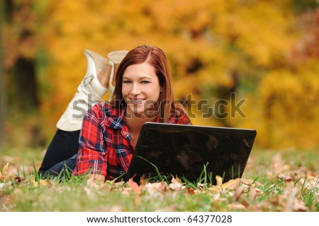 Young Woman laying down with a laptop computer with fall background out of focus