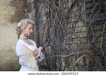 Portrait of a beautiful blonde in an old white satin dress and pearl necklace