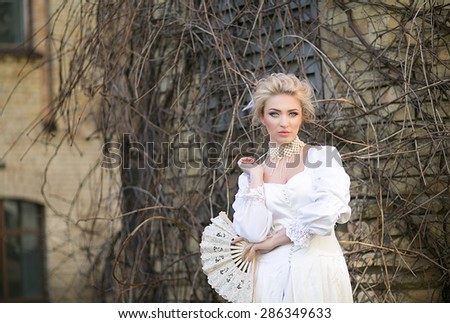 Portrait of a beautiful blonde in an old white satin dress and pearl necklace