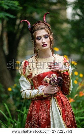 Beautiful young woman in an old dress with red horns on his head, volshbeny garden, fairy tale character