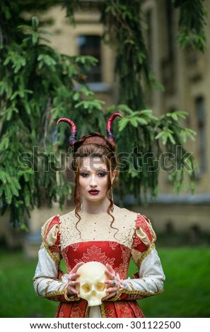 Beautiful girl with demonic horns and skull in his hand, in medieval dress on a background of nature