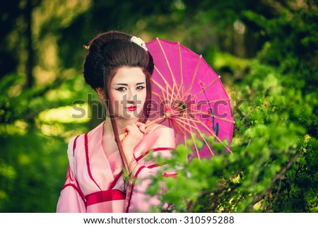 Beautiful Japanese woman in national dress with a pink kimono umbrella gulei of spring green garden, Asia