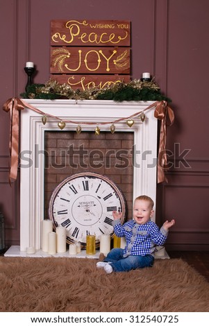 Little boy with a golden Christmas tree ball in hands sitting on the furs by the fire, New Year, Christmas, holiday