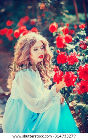 Beautiful young woman with long curls in a long dress the color of mint in the summer garden with roses