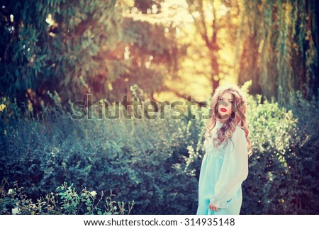 Lovely young woman in a long dress the color of mint with long curly hair in a summer garden