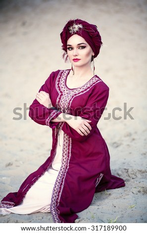Portrait of a beautiful woman with make-up in the Arab east suit and turban, sitting in the desert