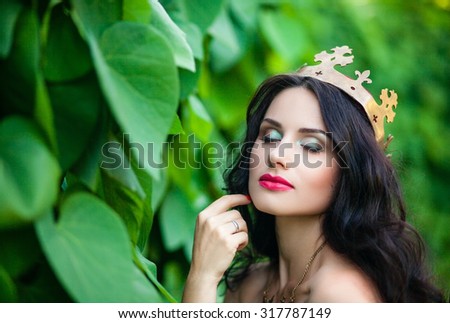 Portrait of a beautiful princess with a golden crown, a red dress and long black hair, a walk through the garden, closeup