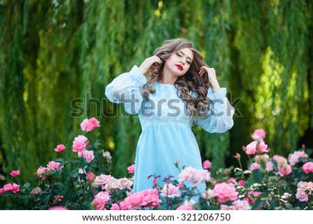 Beautiful girl in a long dress the color of mint walk on summer garden among the blooming roses