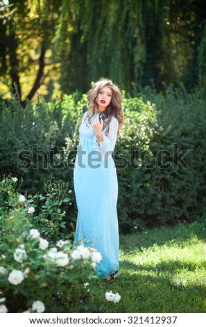 Beautiful young woman in a long dress the color of mint walk on summer garden among the blooming roses