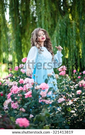 Beautiful girl in a long dress the color of mint walk on summer garden among the blooming roses