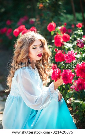 Beautiful young long-haired girl in a dress the color of mint gentle smell the pink rose in the summer garden