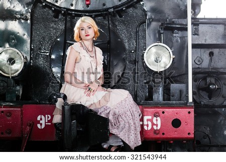 Beautiful feminine blonde girl in a vintage dress near the vintage train at the station