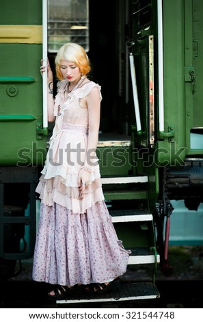 Beautiful feminine blonde girl in a vintage dress near the vintage train at the station