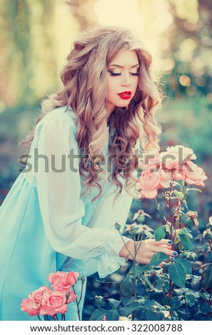 Beautiful young long-haired girl in a dress the color of mint gentle smell the pink rose in the summer garden