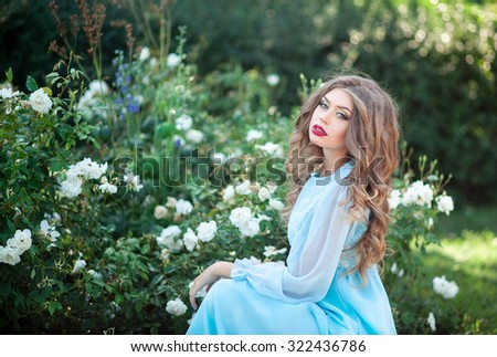 Lovely young woman in a flower bed near the lush garden of white roses, summer, sunset