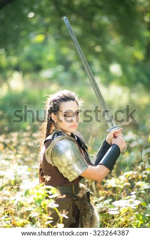 Beautiful amazon warrior in a leather dress with fur and a heavy iron sword in the woods