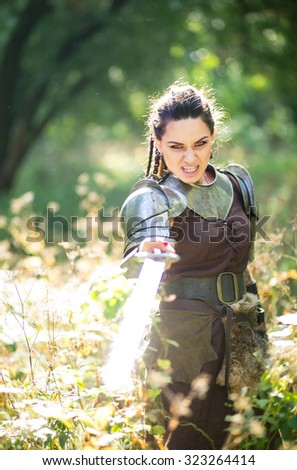 Beautiful amazon warrior in a leather dress with fur and a heavy iron sword in the woods