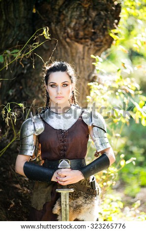 Beautiful dark-haired amazon warrior in dostpehah and sword otdyhavet near a tree