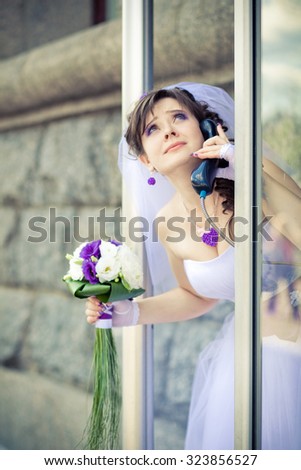 Beautiful bride talking on the phone in the phone booth, wedding day