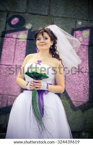 Beautiful bride in a cute dress pinup posing near graffiti painted wall, summer wedding