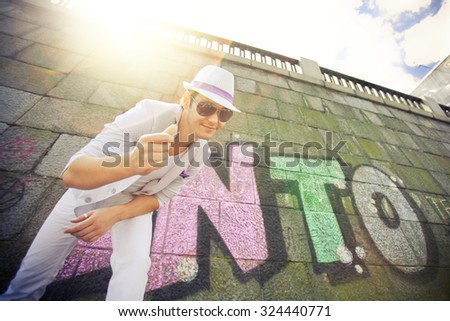 Elegant cheerful young man posing against a wall with graffiti, summer, sunset