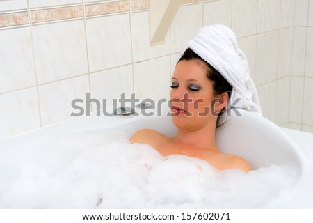 A woman is enjoying a hot bath with a towel around her hair