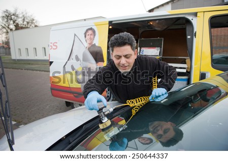 ENSCHEDE, THE NETHERLANDS - 21 NOV, 2014:  A serviceman from \'carglass\' is repairing a crack in the windshield of a car on location