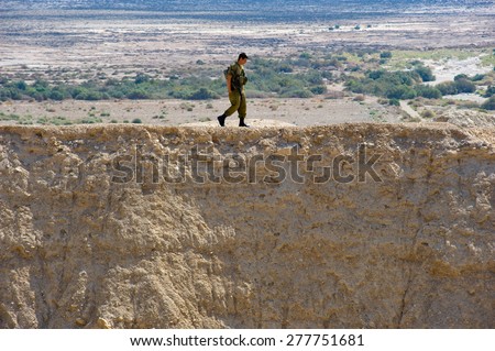DEAD SEA, ISRAEL - OCT 15, 2014: Israeli soldier walking alone on a hill in front of the dead sea in Israel close to Qumran